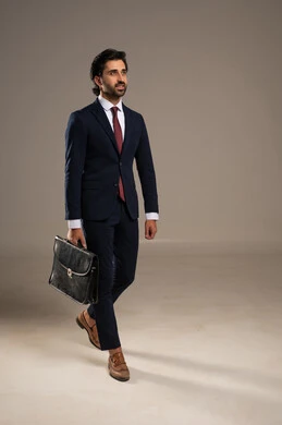 Success and seriousness in work, refined taste and daily practicality, standing with confidence and stability, attention to appearance and self-confidence, a portrait of an Arab Gulf Saudi businessman wearing a formal suit, standing and holding a leather briefcase, white background.