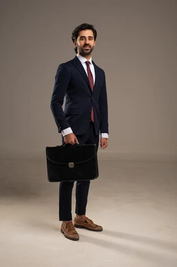أثناء التنقل في رحلة عمل، الذوق الرفيع والعملية اليومية، الوقوف بثقة وثبات، الاهتمام بالمظهر الخارجي والثقة بالنفس، بورتريه لرجل أعمال عربي خليجي سعودي يرتدي البدلة الرسمية يقف  ويحمل حقيبة أعمال جلدية,  خلفية بيضاء