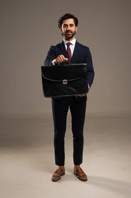 الاحترافية والثقة وتنظيم الحياة العملية، الوقوف بثقة وثبات، الاهتمام بالمظهر الخارجي والثقة بالنفس، بورتريه لرجل أعمال عربي خليجي سعودي يرتدي البدلة الرسمية يقف  ويحمل حقيبة أعمال جلدية,  خلفية بيضاء