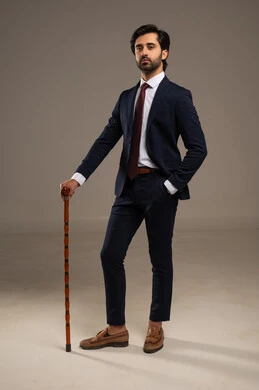 العكاز رمز للمكانة الاجتماعية والذوق الرفيع، الوقوف بثقة وثبات، الاهتمام بالمظهر الخارجي والثقة بالنفس، بورتريه لرجل أعمال عربي خليجي سعودي يرتدي البدلة الرسمية يقف ويحمل عكاز مزخرف مما يضيف يكسر النمط التقليدي,  خلفية بيضاء