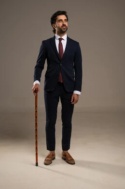 Attention to appearance and self-confidence, use of modern technologies, a portrait of a Saudi Gulf Arab businessman wearing a formal suit standing and holding a decorative cane which adds to breaking the traditional pattern, the cane as an elegant accessory, white background.