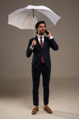 Communication with family and friends through a phone call, winter atmosphere, the concept of protection from rain, using modern technologies, a portrait of an Arab Gulf Saudi businessman wearing a formal suit standing and holding an umbrella and a mobile phone, attention to external appearance, white background.