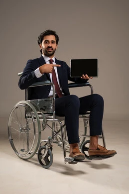 Pointing with the index finger at the mobile device, managing and organizing business affairs through technical devices, integrating work with technology and technology, a portrait of a Saudi Arabian Gulf man with special needs wearing a formal uniform sitting in a wheelchair working on a tablet, white background.