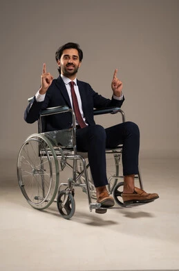 Number one, the lifestyle of people with determination, the support of the Saudi community for the hobbies of people with special needs, enjoying practicing favorite hobbies, a portrait of a Saudi Gulf Arab man in a suit sitting in a wheelchair raising his index fingers upwards, white background.