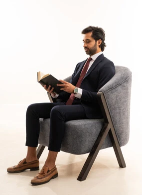 Self-learning and education, the concept of reading and literature, reading skills and increasing awareness, the concept of elegance, beauty, and masculinity, recreational youth activities, a portrait of a young Arab Gulf Saudi man wearing formal attire sitting on a comfortable sofa holding a book flipping through its pages to gain new experiences, white background.