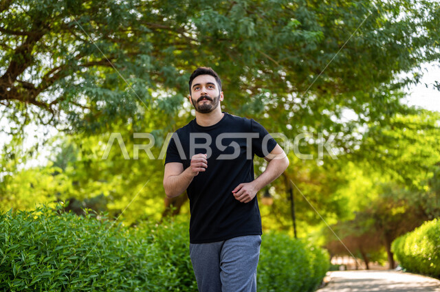 رجل عربي يمارس الرياضة الصباحية في الهواء الطلق ، ممارسة رياضة الجري ، ممارسة الرياضة على طريق الممشى المخصص للمشي بإحدى حدائق السعودية ، نشاط بدني للمحافظة على اللياقة والصحة الجيدة ، ممارسة التمارين الرياضية في وضع النهار