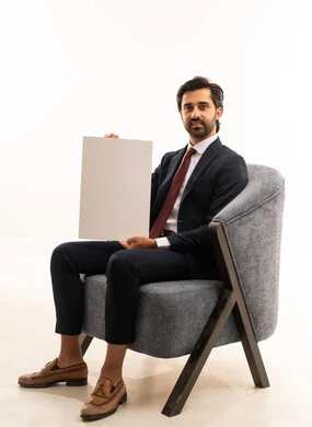 Advertising and marketing campaigns, white rectangular mockup, the concept of elegance, beauty, and masculinity, recreational youth activities, a portrait of a young Arab Gulf Saudi man wearing formal attire sitting on a comfortable sofa holding a white rectangular board, white background.