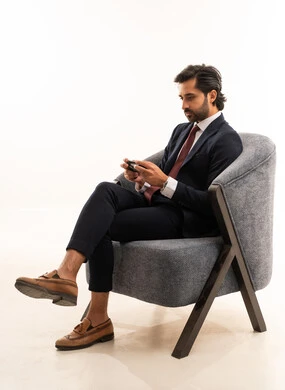Interaction and immersion with video games, spending leisure time playing video games, recreational youth activities, a portrait of a young Arab Gulf Saudi man wearing formal attire sitting on a comfortable sofa holding a game controller and playing video games, the concept of beauty, elegance, and masculinity, white background.
