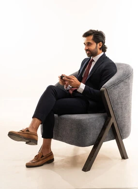 Spending leisure time playing video games, recreational youth activities, interacting and engaging with video games, a portrait of a young Arab Gulf Saudi man wearing formal attire sitting on a comfortable sofa holding a game controller and playing video games, the concept of beauty, elegance, and masculinity, white background.