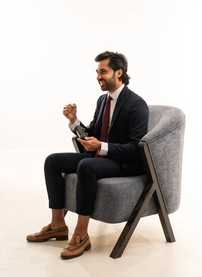 Expressions of victory in a game, interaction and immersion with video games, spending leisure time playing video games, recreational youth activities, a portrait of a young Arab Gulf Saudi man wearing formal attire sitting on a comfortable sofa holding a game controller and playing video games, white background.