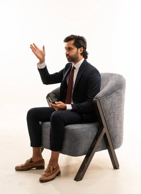 تعابير الخسارة في احدى الألعاب، التفاعل والاندماج مع ألعاب الفيديو،  قضاء اوقات الفراغ باللعب بالعاب الفيديو، أنشطة شبابية ترفيهية، بورتريه لشاب عربي خليجي سعودي يرتدي الطقم الرسمي ويجلس على اريكة مريحة يحمل عصا تحكم ويلعب العاب الفيديو, خلفية بيضاء