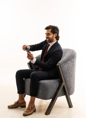 أنشطة شبابية ترفيهية، قضاء اوقات الفراغ باللعب بالعاب الفيديو، التفاعل والاندماج مع ألعاب الفيديو، , بورتريه لشاب عربي خليجي سعودي يرتدي الطقم الرسمي ويجلس على اريكة مريحةيحمل عصا تحكم ويلعب العاب الفيديو, مفهوم الجمال والاناقة والرجولة، خلفية بيضاء