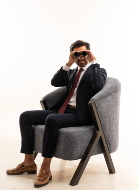 The concept of exploration and adventure, searching for something and expanding the field of vision using binoculars, future visions among youth, a portrait of a young Arab Gulf Saudi man wearing formal attire sitting on a comfortable sofa and looking through binoculars, a Saudi man searching and exploring, white background.
