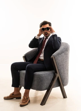 Future visions among youth, the concept of exploration and adventure, searching for something and expanding the field of vision using binoculars, a portrait of a young Arab Gulf Saudi man wearing formal attire sitting on a comfortable sofa and looking through binoculars, a Saudi man searching and exploring, white background.