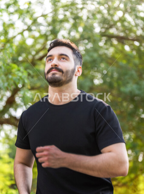 رجل عربي يمارس الرياضة الصباحية في الهواء الطلق ، ممارسة رياضة الجري ، ممارسة الرياضة على طريق الممشى المخصص للمشي بإحدى حدائق السعودية ، نشاط بدني للمحافظة على اللياقة والصحة الجيدة ، ممارسة التمارين الرياضية في وضع النهار