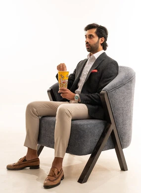 Spending free time watching entertaining movies and series, having a healthy and light snack, a portrait of a Saudi Arabian Gulf man wearing a formal suit sitting on a comfortable sofa and eating popcorn, white background.