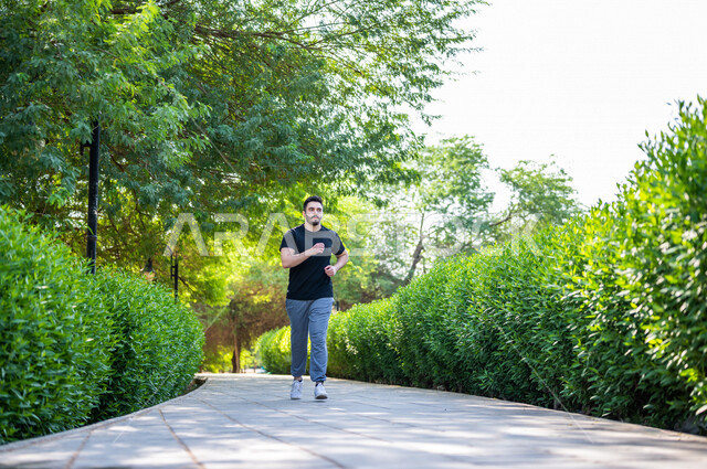 رجل عربي يمارس الرياضة الصباحية في الهواء الطلق ، ممارسة رياضة الجري ، ممارسة الرياضة على طريق الممشى المخصص للمشي بإحدى حدائق السعودية ، نشاط بدني للمحافظة على اللياقة والصحة الجيدة ، ممارسة التمارين الرياضية في وضع النهار