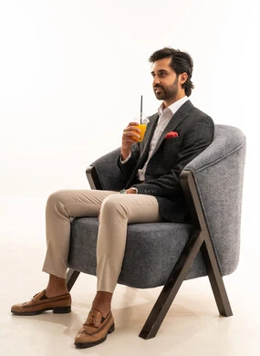 Trying to alleviate the summer heat with a refreshing drink, enjoying delicious and beneficial beverages, a portrait of a smiling Arab Gulf Saudi man wearing a formal suit sitting on a comfortable chair and enjoying a cold natural juice, white background.