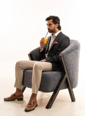Trying to alleviate the summer heat with a refreshing drink, enjoying delicious and beneficial beverages, a portrait of a smiling Arab Gulf Saudi man wearing a formal suit sitting on a comfortable chair and enjoying a cold natural juice, white background.
