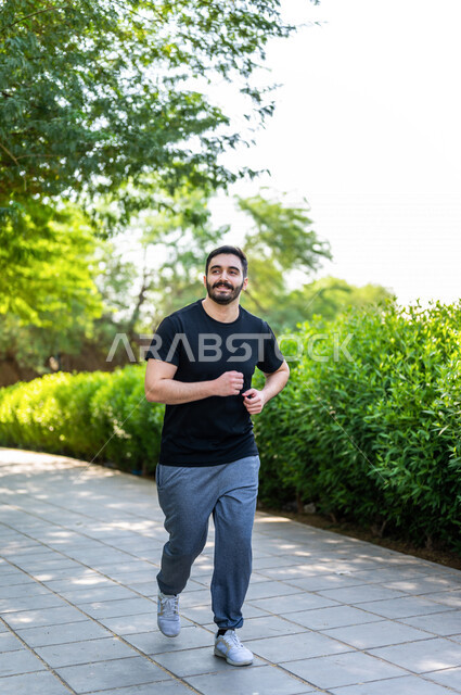 رجل عربي يمارس الرياضة الصباحية في الهواء الطلق ، ممارسة رياضة الجري ، ممارسة الرياضة على طريق الممشى المخصص للمشي بإحدى حدائق السعودية ، نشاط بدني للمحافظة على اللياقة والصحة الجيدة ، ممارسة التمارين الرياضية في وضع النهار