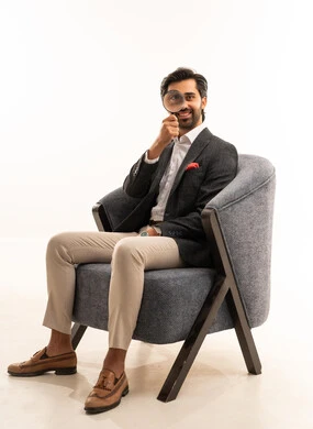 عمليات البحث والتدقيق، مضاعفة الأحجام ومحاولة إيجاد الأشياء الصغيرة، بورتريه لرجل عربي خليجي سعودي يرتدي البدلة الرسمية يجلس على كرسي يحاول اكتشاف شيء ما باستخدام العدسة المكبرة، إيماءات الاندماج والسرور، تكبير وتوضيح الرؤية، خلفية بيضاء