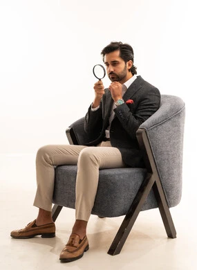 Search and inspection operations, magnifying sizes and trying to find small things, a portrait of a Saudi Arabian Gulf man in formal attire sitting on a chair trying to discover something using a magnifying glass, gestures of engagement and pleasure, magnifying and clarifying vision, white background.