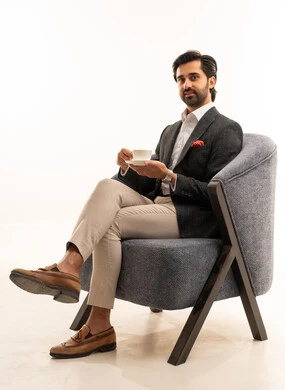 Drinking his favorite beverage, a portrait of an Arab Gulf Saudi businessman wearing a formal suit sitting on a comfortable chair holding a white coffee cup and a small plate, his facial expressions are calm and smiling, attention to appearance, white background.