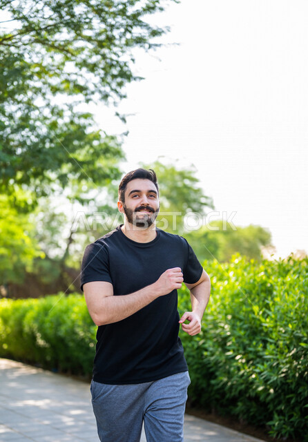 رجل عربي يمارس الرياضة الصباحية في الهواء الطلق ، ممارسة رياضة الجري ، ممارسة الرياضة على طريق الممشى المخصص للمشي بإحدى حدائق السعودية ، نشاط بدني للمحافظة على اللياقة والصحة الجيدة ، ممارسة التمارين الرياضية في وضع النهار