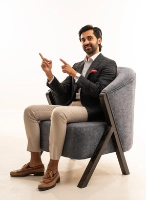 Pointing with the index finger at something, gestures and expressions of joy and happiness, the concept of elegance and masculinity, a portrait of an Arab Gulf Saudi businessman wearing a formal suit sitting on a comfortable chair, attention to external appearance, white background.