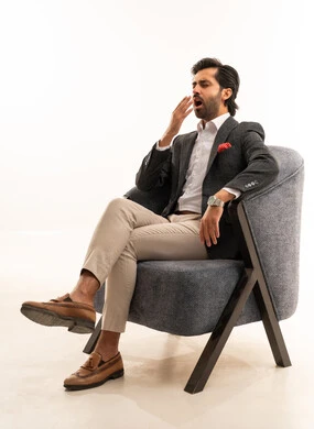The need for rest and sleep, the feeling of fatigue from work pressure, a portrait of a Saudi Arabian Gulf man wearing a formal suit sitting on a comfortable chair raising his hands with gestures of yawning and drowsiness, white background.