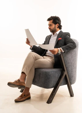 Reviewing notes, preparing work-related reports, a portrait of a Saudi Gulf Arab man in formal attire sitting on a comfortable chair holding a stack of white papers, reviewing and following up on office plans and projects with focused gestures, white background.
