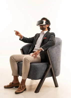 Simulation of the imaginary world, a young Saudi man pointing to a place with expressions of immersion and simulation of the imaginary world, attempting to click on something, a portrait of an Arab Gulf Saudi man wearing a formal suit sitting on a comfortable chair wearing 3D glasses raising his index finger upwards, white background.