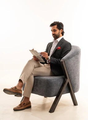 Preparing work-related reports, checking the reading of notes, a portrait of a Saudi Arabian Gulf man in formal attire sitting on a comfortable chair holding papers, reviewing and following up on office plans and projects with focused gestures, white background.