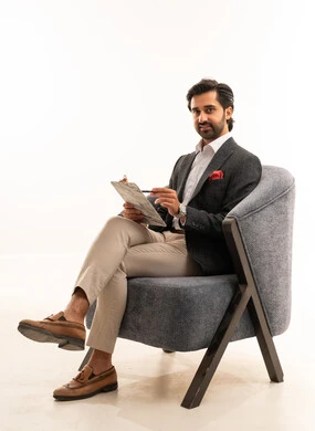 اعداد التقارير الخاصة بالعمل، التدقيق في قراءة الملاحظات، بورتريه لرجل عربي خليجي سعودي يرتدي البدلة الرسمية يجلس على كرسي مريح يحمل بيده اوراق، مراجعة ومتابعة الخطط والمشاريع المكتبية بإيماءات التركيز، خلفية بيضاء