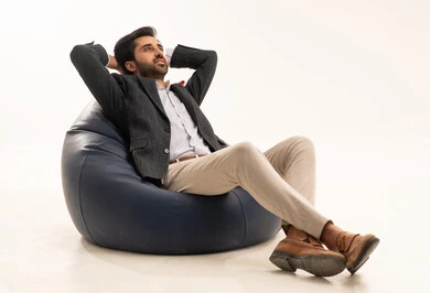 The need for rest and sleep, the feeling of fatigue from work pressure, a portrait of a Saudi Arabian Gulf man wearing a formal suit sitting on a comfortable chair, raising his hands behind his head in relaxation gestures, white background.