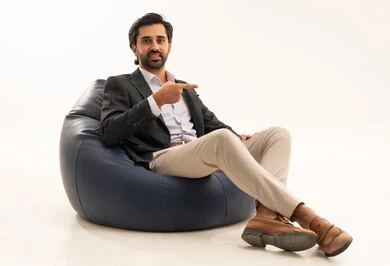 الإشارة بإصبع السبابة إلى شيء ما، الاهتمام بالمظهر الخارجي، مفهوم الاناقة والرجولة، بورتريه لرجل أعمال عربي خليجي سعودي يرتدي البدلة الرسمية يجلس على كرسي بين بادج مريح، خلفية بيضاء