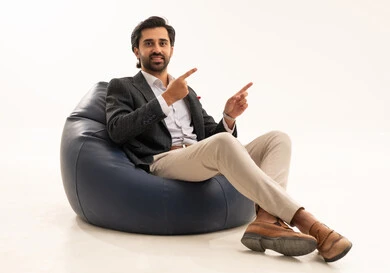 Pointing with the index finger at something, concern for external appearance, the concept of elegance and masculinity, a portrait of an Arab Gulf Saudi businessman wearing a formal suit sitting on a chair between comfortable cushions, white background.