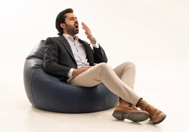 الحاجة إلى الاستراحة والنوم, الشعور بالتعب من ضغط العمل، بورتريه لرجل عربي خليجي سعودي يرتدي البدلة الرسمية يجلس على كرسي مريح يرفع يدي بإيماءات التثاؤب والنعاس، خلفية بيضاء