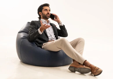 اجراء مكالمة هاتفية عبر الجوال، دمج التكنولوجيا في الحياة العملية، استخدام تقنية حديثة ومتطورة، إدارة شؤون العمل وتنظيمها عبر الإنترنت، بورتريه لرجل اعمال عربي خليجي سعودي يرتدي البدلة الرسمية يجلس على كرسي بين بادج مريح يحمل بيده الهاتف المحمول, خلفية بيضاء