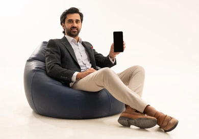 عرض شاشة سوداء فارغة عبر الجوال، دمج التكنولوجيا في الحياة العملية، استخدام تقنية حديثة ومتطورة، إدارة شؤون العمل وتنظيمها عبر الإنترنت، بورتريه لرجل اعمال عربي خليجي سعودي يرتدي البدلة الرسمية يجلس على كرسي بين بادج مريح يحمل بيده الهاتف المحمول, خلفية بيضاء