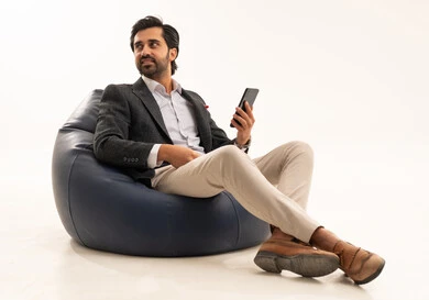 Using modern and advanced technology, integrating technology into practical life, managing and organizing work affairs online, a portrait of an Arab Gulf Saudi businessman wearing a formal suit sitting on a chair in a comfortable badge holding a mobile phone in his hand, white background.