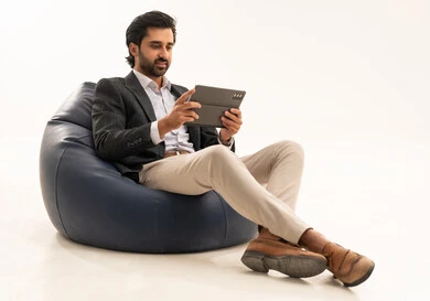 Integrating technology into practical life, using modern and advanced technology, managing and organizing work affairs online, a portrait of an Arab Gulf Saudi businessman wearing a formal suit sitting on a chair in a comfortable lounge holding a tablet in his hand, white background.