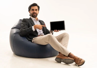 عرض شاشة سوداء فارغة ، دمج التكنولوجيا في الحياة العملية، استخدام تقنية حديثة ومتطورة، إدارة شؤون العمل وتنظيمها عبر الإنترنت، بورتريه لرجل اعمال عربي خليجي سعودي يرتدي البدلة الرسمية يجلس على كرسي بين بادج مريح يحمل بيده التابليت المحمول, خلفية بيضاء