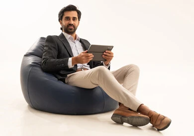 دمج التكنولوجيا في الحياة العملية، استخدام تقنية حديثة ومتطورة، إدارة شؤون العمل وتنظيمها عبر الإنترنت، بورتريه لرجل اعمال عربي خليجي سعودي يرتدي البدلة الرسمية يجلس على كرسي بين بادج مريح يحمل بيده التابليت المحمول, خلفية بيضاء