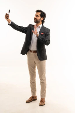 Taking a commemorative selfie via mobile, integrating technology into practical life, using modern and advanced technology, managing and organizing work affairs online, a portrait of an Arab Gulf Saudi businessman wearing a formal suit holding a mobile phone in his hand, full body, white background.