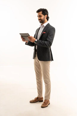 Using modern and advanced technology, managing and organizing business affairs, holding an online business meeting, a portrait of an Arab Gulf Saudi businessman wearing a formal suit holding a tablet in his hand, integrating technology into practical life, full-body, white background.