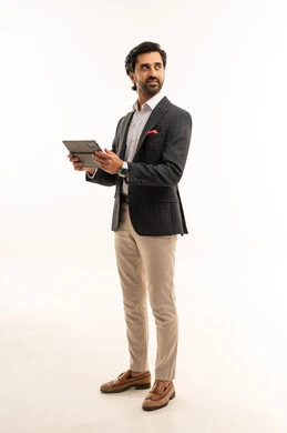 Using modern and advanced technology, managing and organizing business affairs, holding an online business meeting, a portrait of an Arab Gulf Saudi businessman wearing a formal suit holding a tablet in his hand, integrating technology into practical life, full-body, white background.
