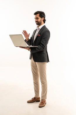 إدارة شؤون الأعمال وتنظيمها، استخدام التقنيات الحديثة المتطورة، عقد إجتماع عمل عبر الإنترنت، بورتريه لرجل اعمال عربي خليجي سعودي يرتدي البدلة الرسمية يقوم بالعمل على الحاسب المحمول, دمج التكنولوجيا في الحياة العملية، الجسم بالطول الكامل، خلفية بيضاء