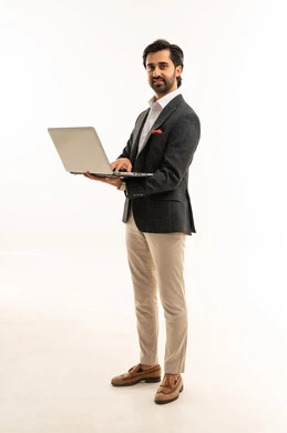 إدارة شؤون الأعمال وتنظيمها، استخدام التقنيات الحديثة المتطورة، عقد إجتماع عمل عبر الإنترنت، بورتريه لرجل اعمال عربي خليجي سعودي يرتدي البدلة الرسمية يقوم بالعمل على الحاسب المحمول, دمج التكنولوجيا في الحياة العملية، الجسم بالطول الكامل، خلفية بيضاء