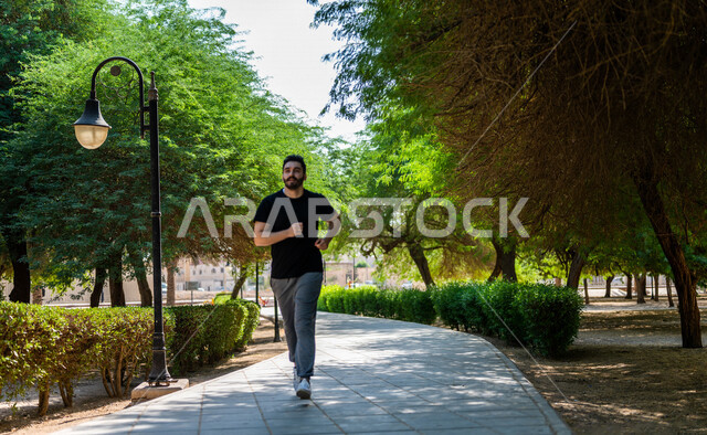 رجل عربي يمارس الرياضة الصباحية في الهواء الطلق ، ممارسة رياضة الجري ، ممارسة الرياضة على طريق الممشى المخصص للمشي بإحدى حدائق السعودية ، نشاط بدني للمحافظة على اللياقة والصحة الجيدة ، ممارسة التمارين الرياضية في وضع النهار